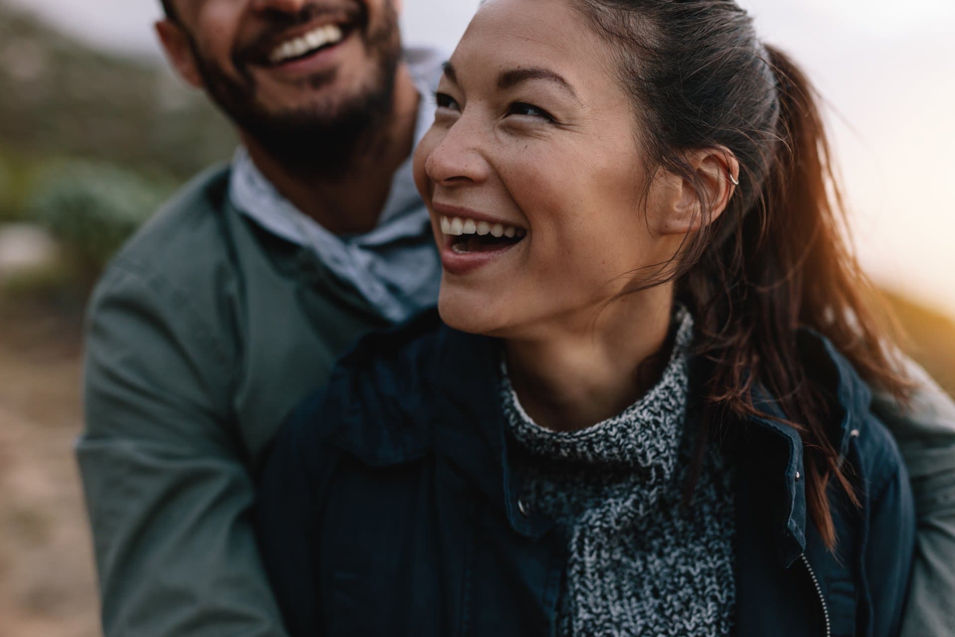 Smiling woman and bearded man laughing together outdoors, representing wellness, healthy living and positive patient outcomes.